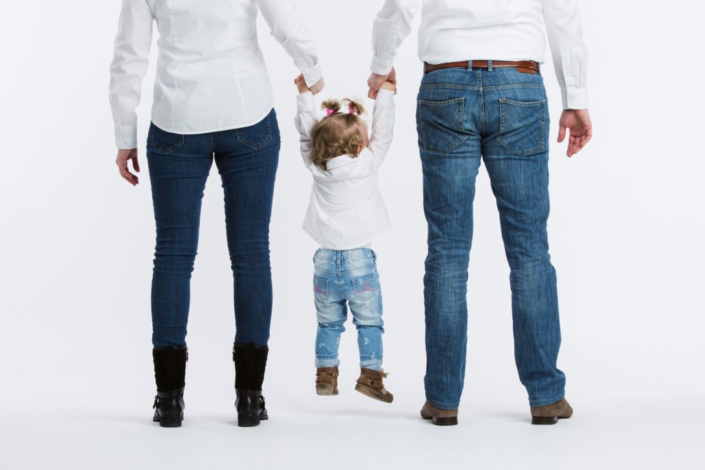 Jasmijn hangend aan de handen van haar ouders met de voeten van de grond en de rug naar de camera gedraaid