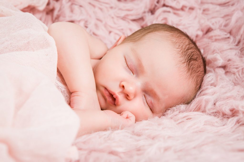 Ize slapend op een newbornkussen op een roze deken gewikkeld in een roze wrap