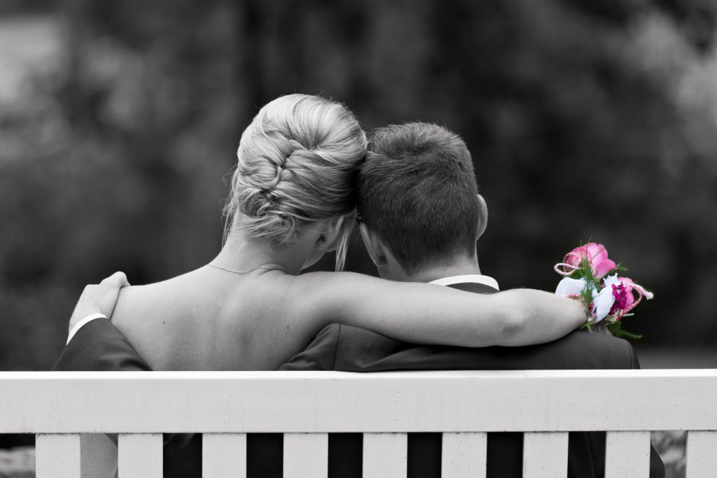 Bruidsfotografie Berry en Saskia op een bankje in de tuin van Kasteel Groot Buggenum in zwart-wit met een roze boeket