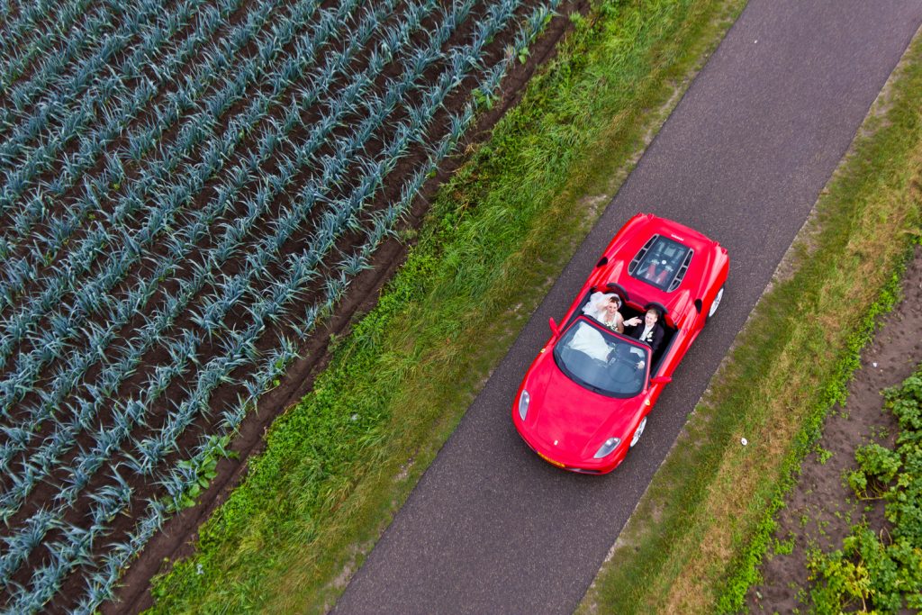 Luchtfoto tijdens bruidsreportage van het koppel in de auto op de weg