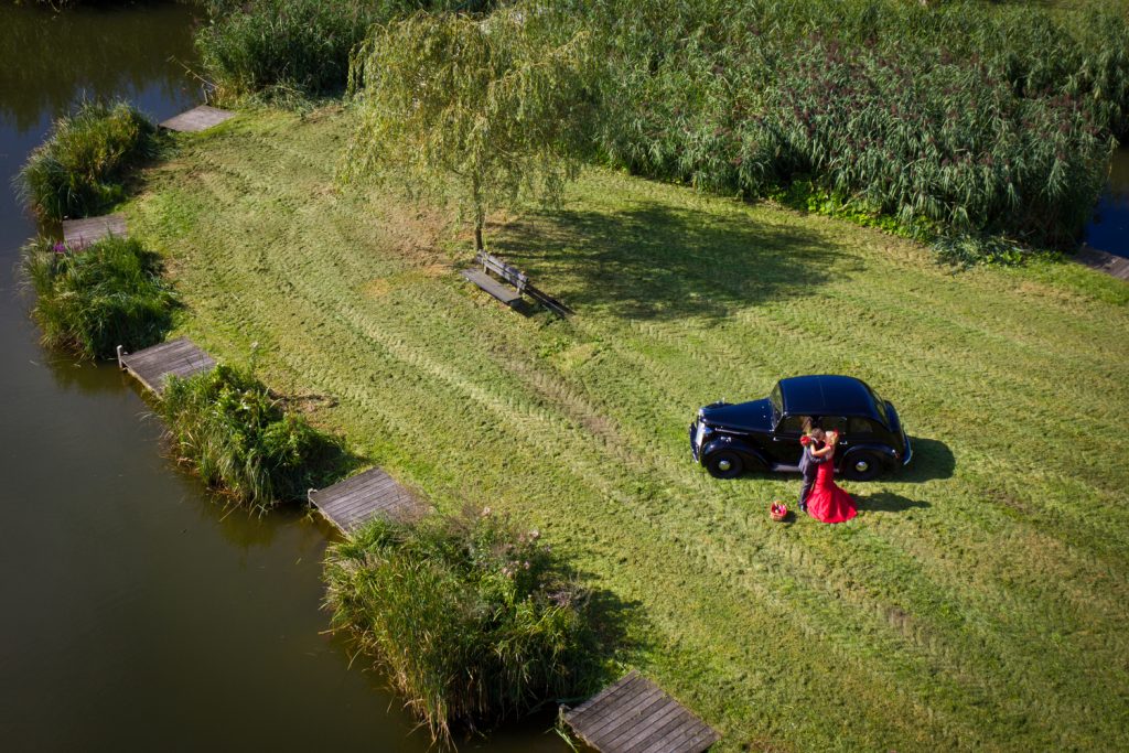 Luchtfoto tijdens bruidsreportage van koppel bij de auto op een grasveld aan het water